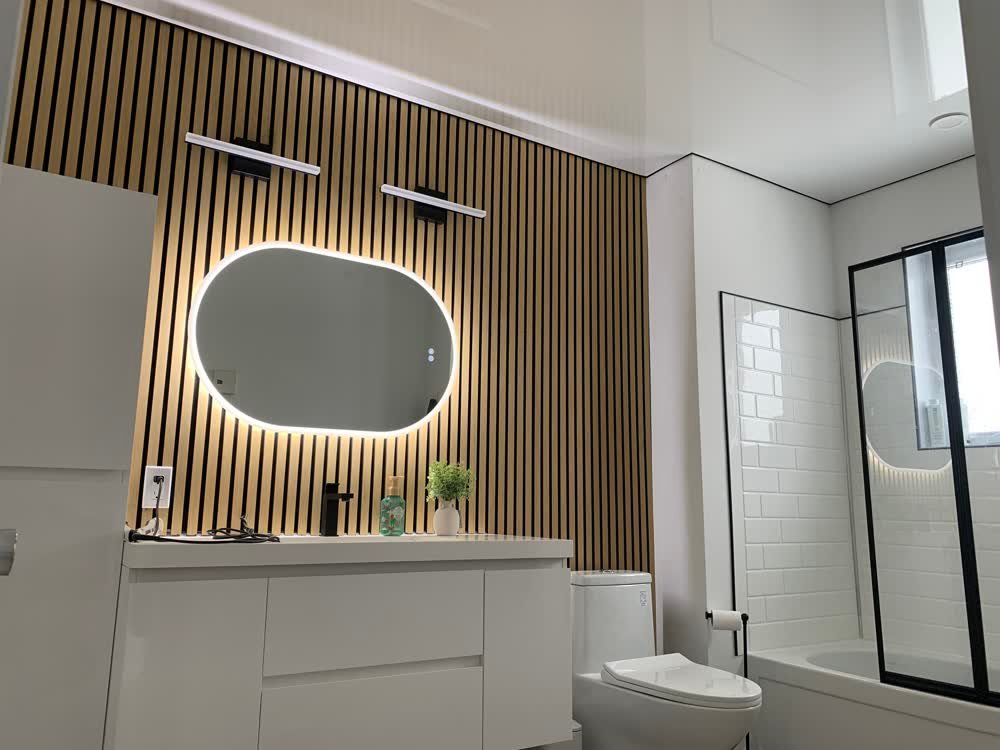 Salle de bain terminée avec mur de tasseaux de bois, miroir rétroeclairé et douche en céramique